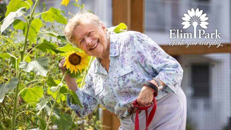 Barbara smiling in the Victory Garden at Elim Park while holding a sunflower.